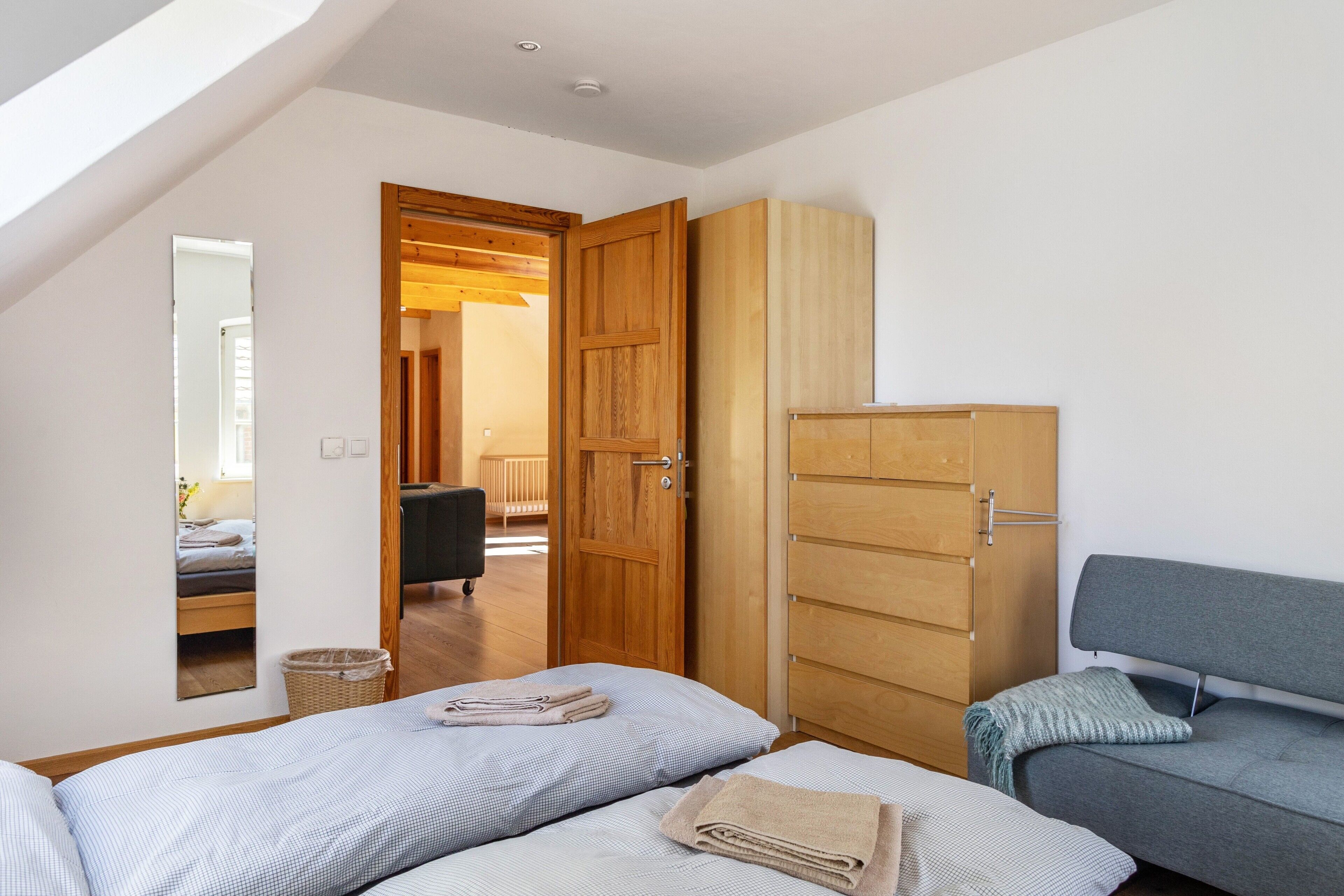 A bedroom with a loft bed, a wardrobe, a sofa, and a mirror.