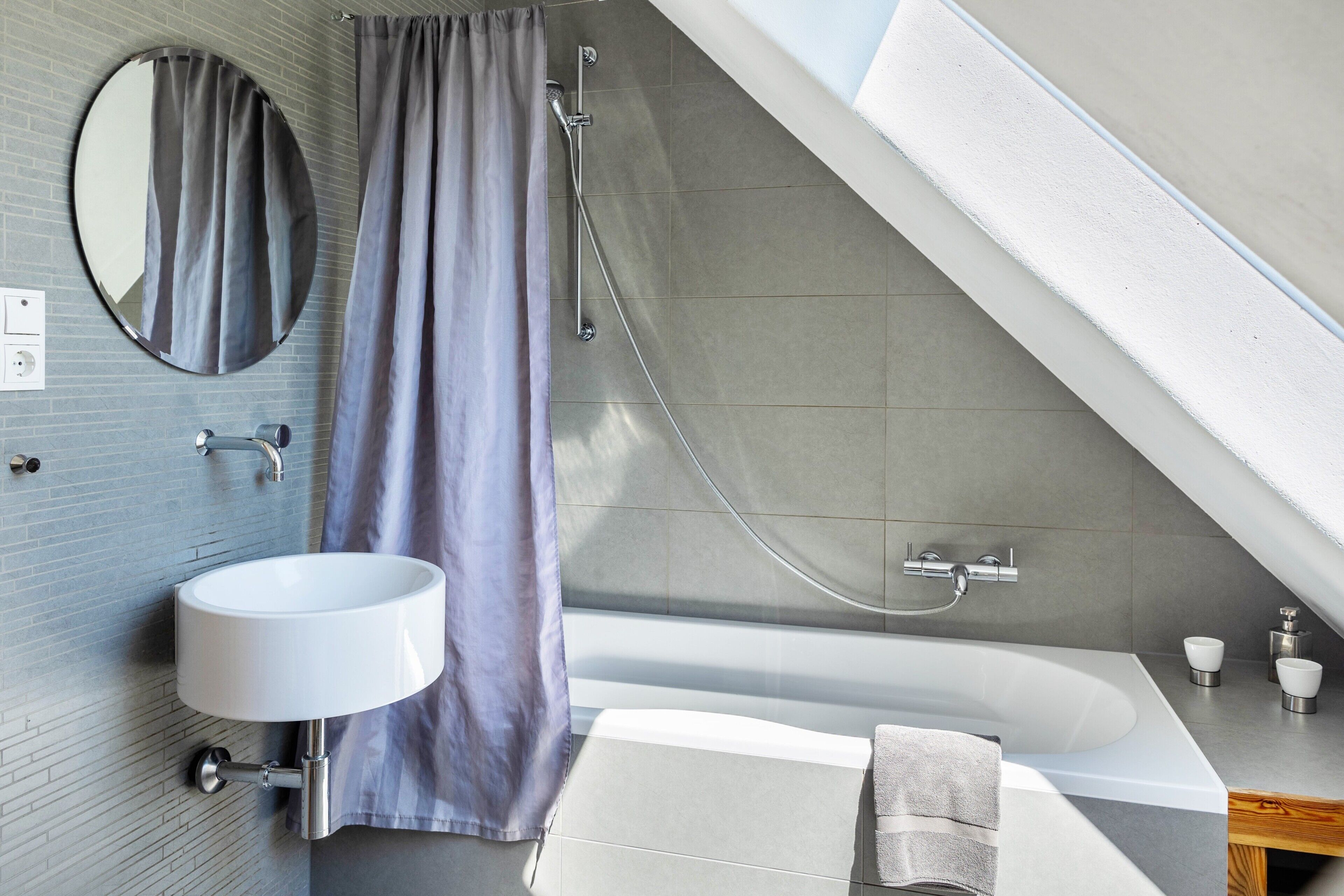 Un baño moderno con bañera, espejo redondo, ducha y lavamanos.