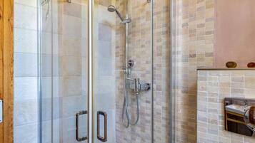 Una ducha con mampara de vidrio, pared con azulejos y un lavamanos pequeño con espejo.