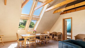 Una habitación con techo inclinado, vigas de madera, una mesa de comedor con sillas, un sofá y un ventanal grande.