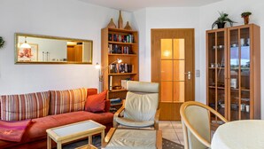 Una sala de estar con sofá, sillón, mesa de centro, estantería y aparador.