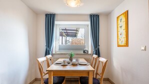 Un coin repas avec une table dressée pour quatre personnes, une plante en pot et une fenêtre avec des rideaux.
