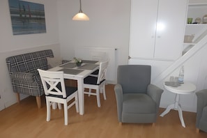 A dining area with a table, chairs, a pendant light, a gray armchair, and a white cabinet.