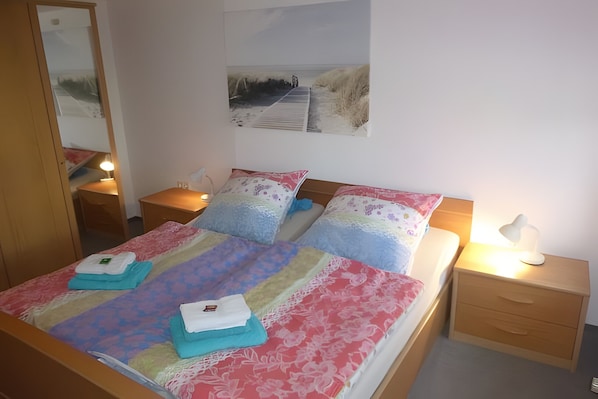 A neatly made bed with a colorful bedspread, two pillows, a bedside lamp, and a nightstand with a lamp.