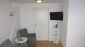 En moderne stue med en grå sofa, et lille rundt bord, en hvid dør og et fjernsyn ophængt på væggen.