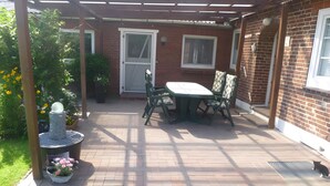 En terrasse med bord og stole, en murstensvæg og et overdækket område med en pergola.
