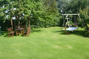 A grassy outdoor area with a wooden swing set and a bench.