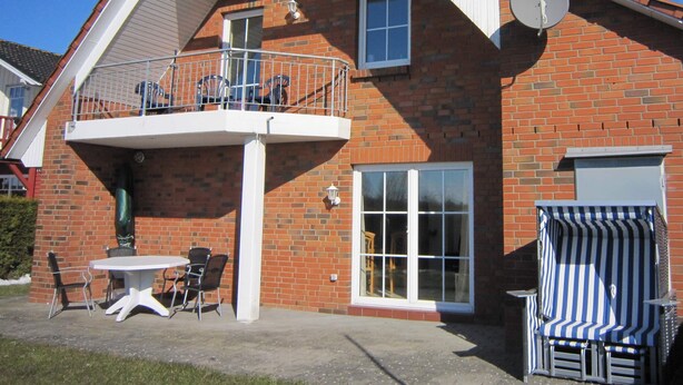 A two-story brick house with a balcony, a satellite dish, and a patio with outdoor furniture. - Apartment ''dat Rode Huus' - Ferienwohnung' with Private Terrace, Private Garden and Wi-Fi (Kronsgaard)