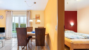 A room with a bed, a dining table with chairs, a TV, and a window with curtains. - Apartment ''dat Rode Huus' - Ferienwohnung' with Private Terrace, Private Garden and Wi-Fi (Kronsgaard)