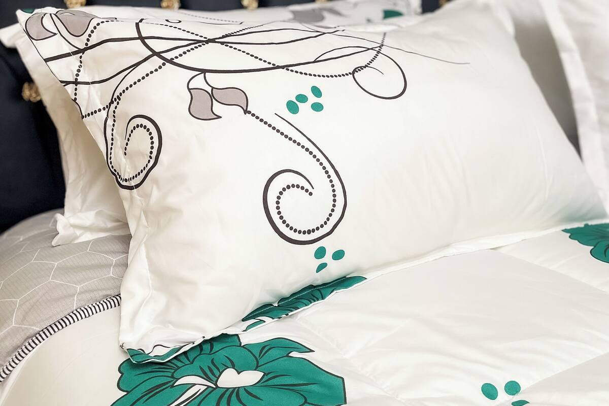 Een bed met een witte spreideken met groene bloemmotieven en een zwart-wit kussen met een bloemenprint.