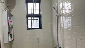 Een kleine, schone badkamer met toilet, raam, douche en zeepdispenser.