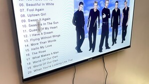 Een televisie waarop een albumhoes met een band en de nummers van de band te zien is.