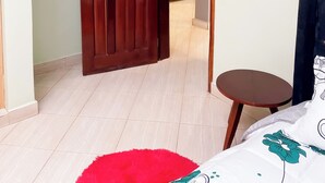 Een kamer met een houten deur, een klein rond tafeltje, een rood vloerkleed en een bed met een bloemenprint.