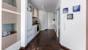 Una cocina moderna con armarios blancos, piso de baldosas oscuras y tres obras de arte en la pared.