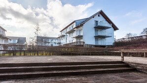 Un edificio residencial de varios pisos con balcones, una terraza de madera y un cielo despejado.