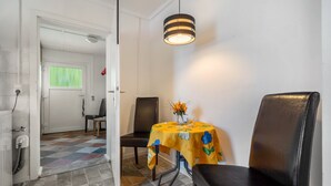 Un coin repas avec une table recouverte d’une nappe jaune, deux chaises, un vase avec des fleurs et un luminaire suspendu.