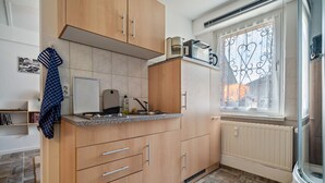 Une cuisine avec des meubles de rangement en bois, un plan de travail, une fenêtre ornée de rideaux en fer forgé et un radiateur.