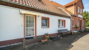 Un bâtiment à l’extérieur blanc, portant le numéro 34, avec une porte, des fenêtres, un banc et des plantes en pot.