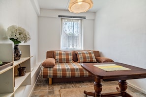 Una habitación acogedora con un sofá a cuadros, una mesa de madera, un jarrón con flores y una ventana con reja decorativa.