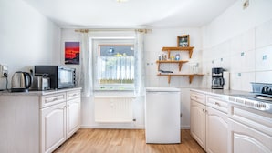 A modern kitchen with white cabinetry, a built-in microwave, a kettle, and a coffee maker. - Apartment 'Fewo Bauer Mecke' with Shared Garden (Mirow)