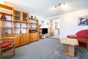 Een woonkamer met houten schap kast, een flatscreen televisie, een rode bank en een kleine houten tafel.