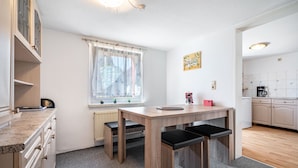 A compact kitchen with a wooden table, two benches, a window with a curtain, and a small kitchen area with cabinets and a coffee machine. - Apartment 'Fewo Bauer Mecke' with Shared Garden (Mirow)