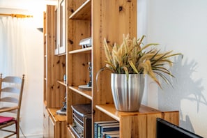 A wooden bookshelf with a metal pot containing plants, a chair, and books. - Apartment 'Fewo Bauer Mecke' with Shared Garden (Mirow)