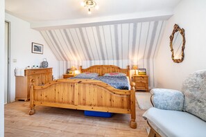 Un dormitorio con techo inclinado, una cama de madera, mesitas de noche, una silla y un espejo.