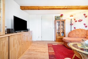 Una sala de estar con televisión, armarios de madera, un sofá, una mesa de centro de vidrio y una alfombra roja.