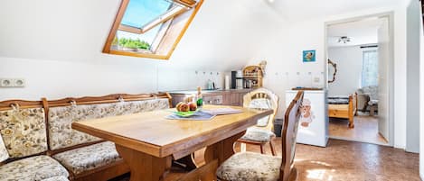 A dining area with a wooden table and bench seating, a kitchen in the background, and a doorway leading to another room.