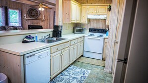 A compact kitchen with wooden cabinets, a dishwasher, a stove, and a microwave. - Recently renovated, beautiful chalet just miles from Wild Animal Safari (Pine Mountain)