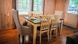 A wooden-paneled dining room with a table set for four, two patterned chairs, and a door with a window view. - Recently renovated, beautiful chalet just miles from Wild Animal Safari (Pine Mountain)