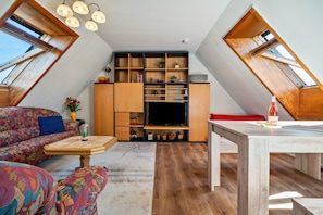 Un espacio tipo loft con sofá, una mesa de comedor, televisor y estantería.