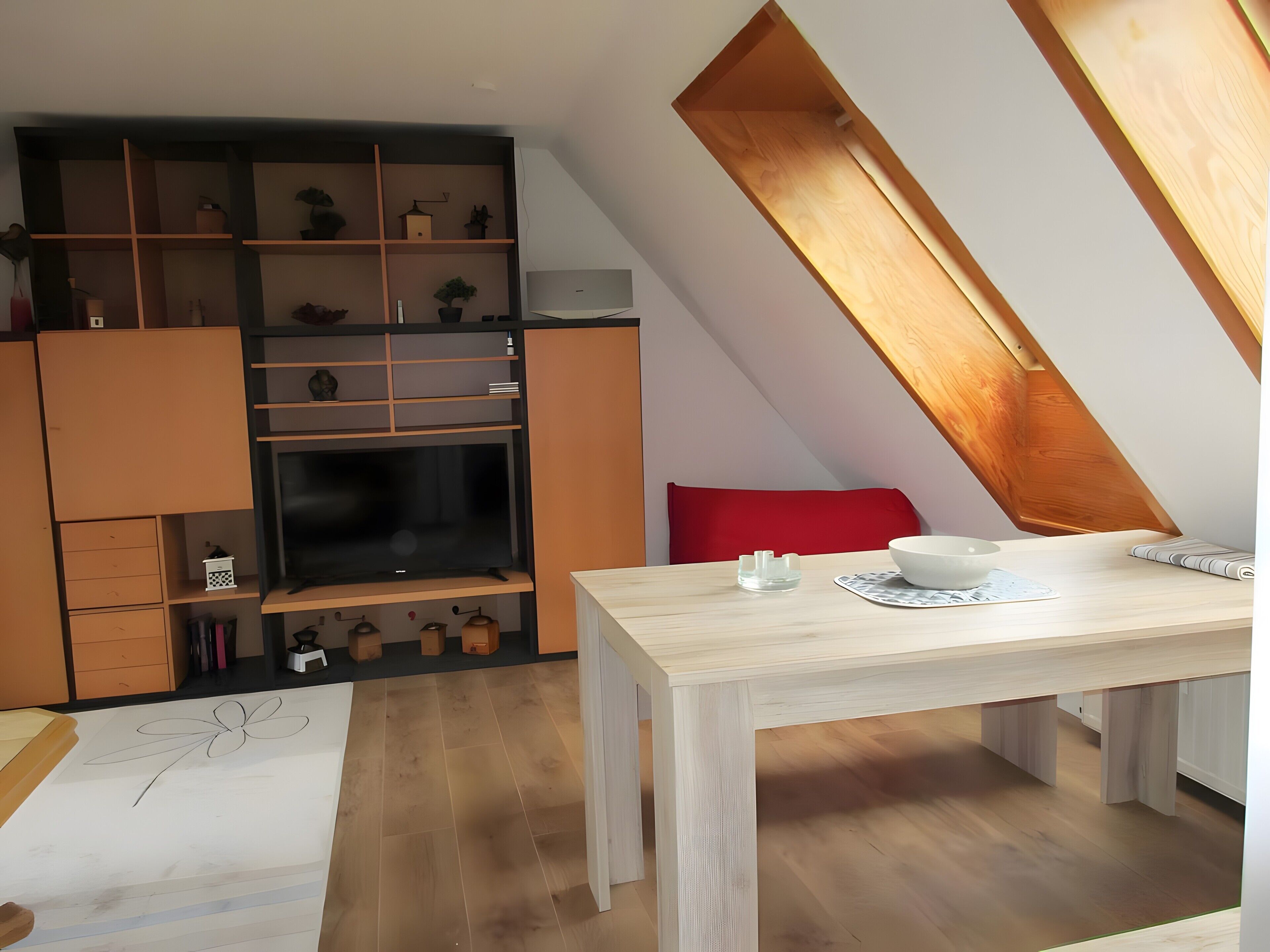 Ein modernes Schlafzimmer im Loft-Stil mit schrägem Dach, integrierten Regalen, einem Esstisch und einer roten Akzentwand.