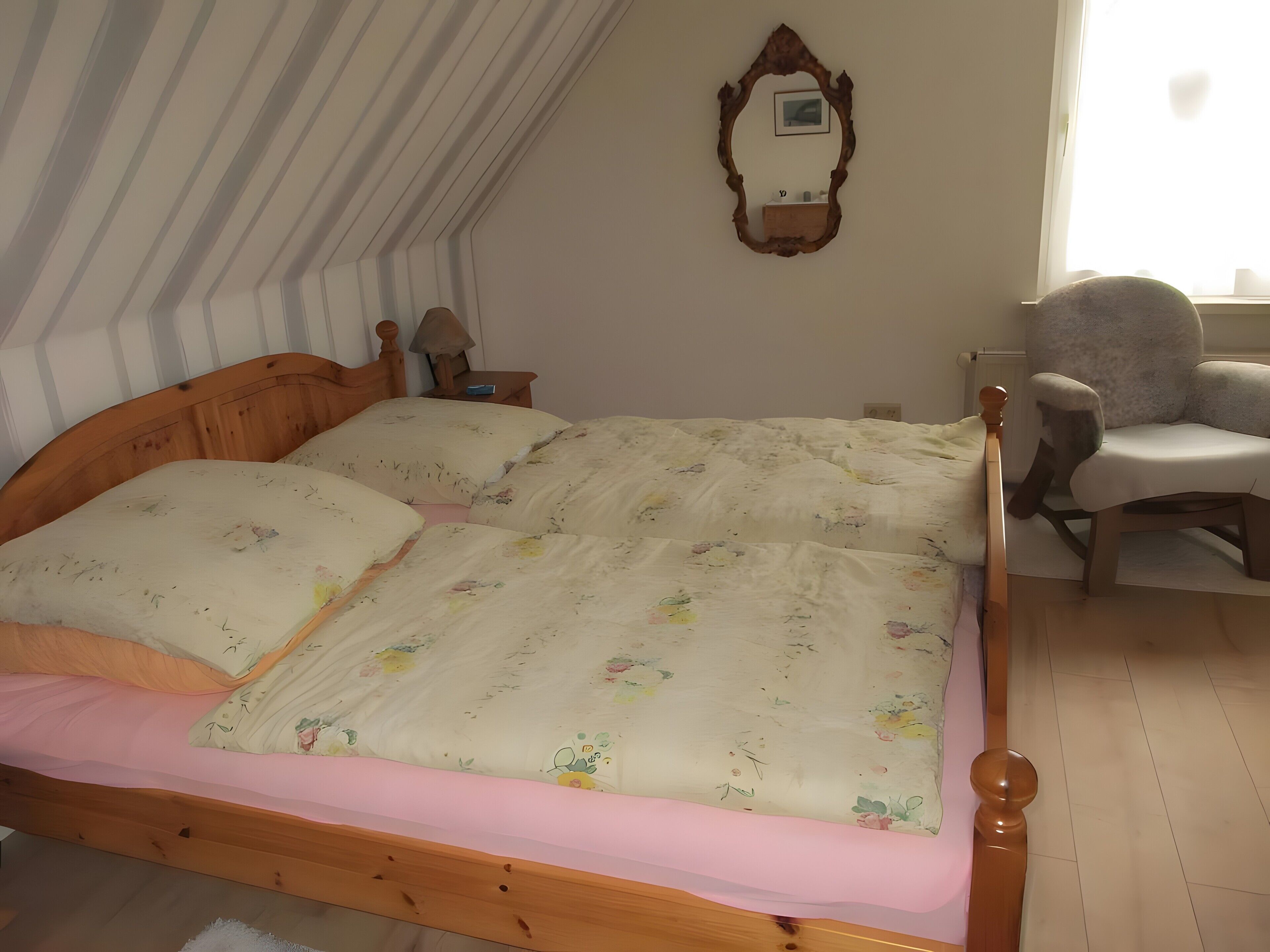 A bedroom with a wooden bed, a chair, a mirror, and a window.