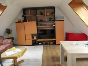 Un espacio habitable compacto con televisor, estanterías de madera, un sofá rojo y una mesa de comedor.
