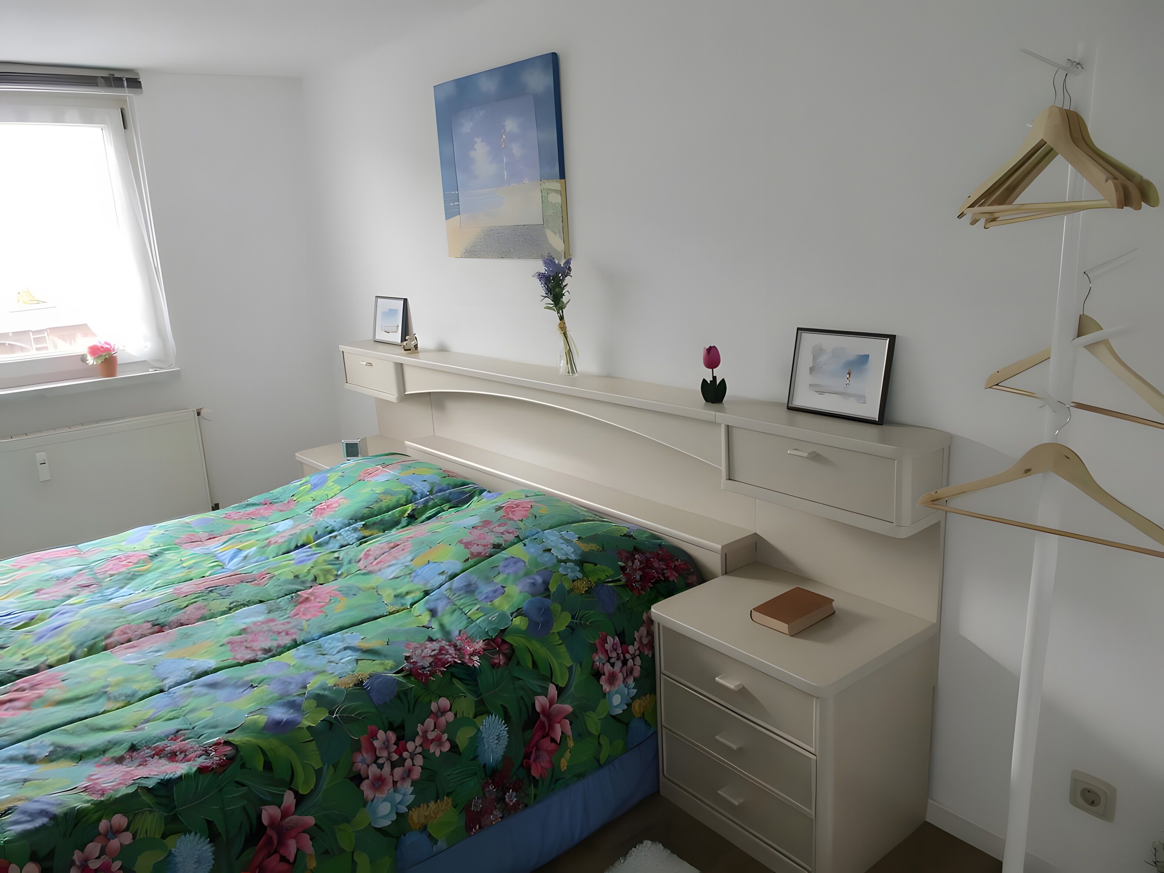 Une chambre à coucher comprenant un lit, des tables de chevet, une commode, une fenêtre avec un rideau et un tableau accroché au mur.