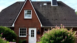 Una casa de dos pisos con techo pronunciado, una chimenea central y una puerta principal con un pequeño ventanal encima.