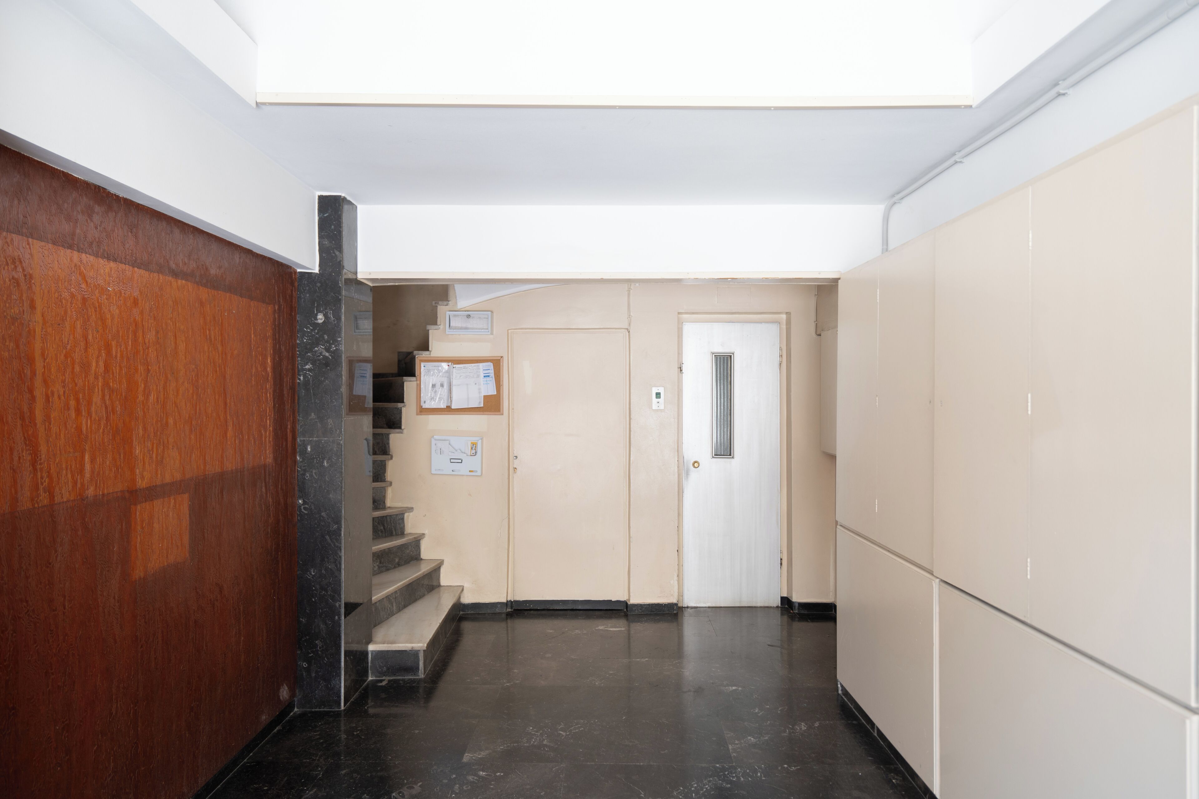Un pasillo con pared de madera, escaleras de mármol y una puerta con rejilla.