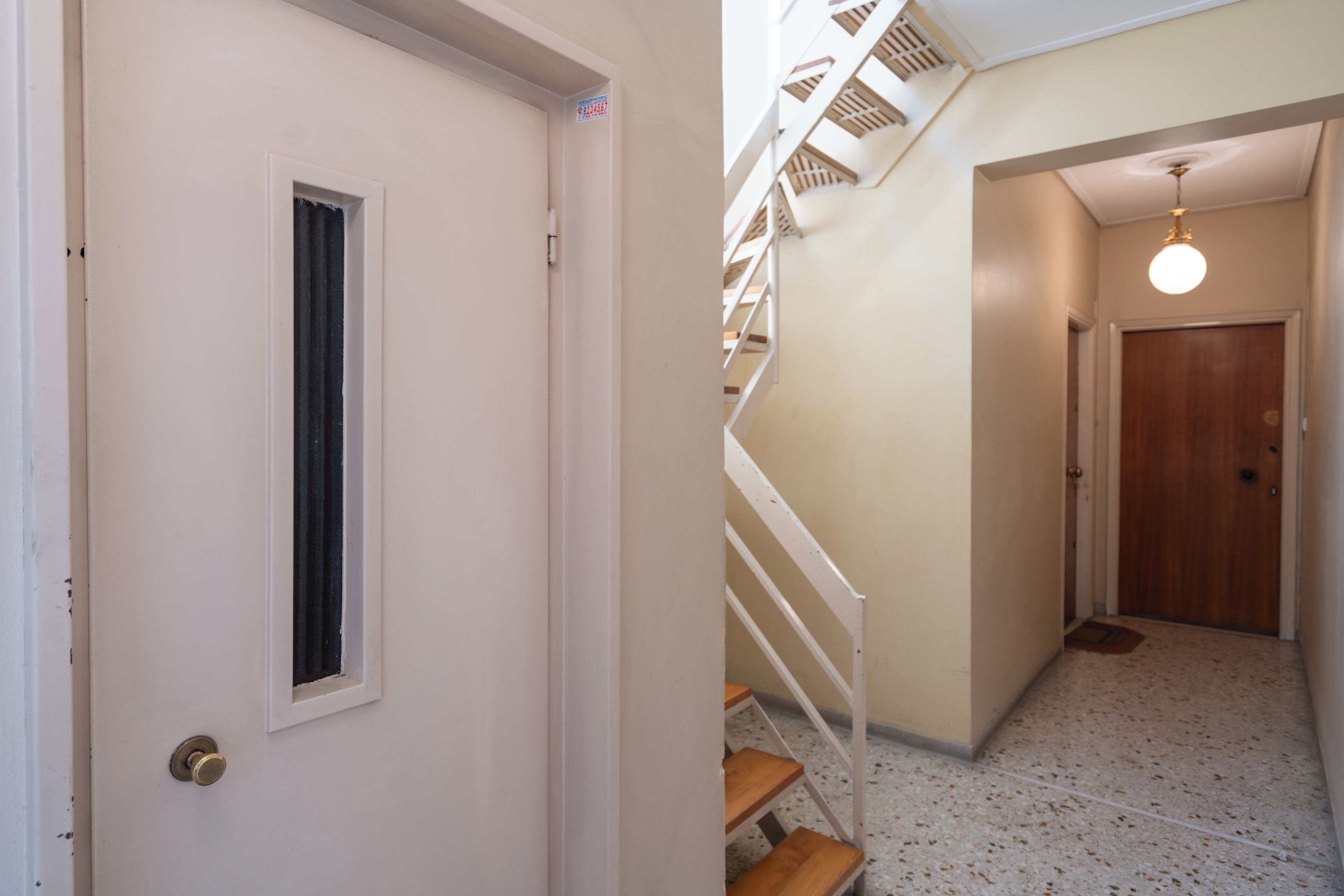 A hallway with a white door, a window, a staircase with white railings, and a wooden door at the end.