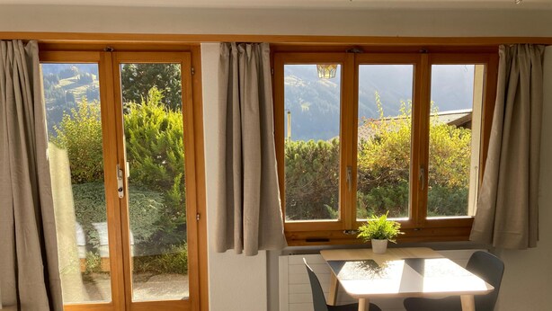 Una habitación con puerta corredera de madera, una mesa con sillas y vistas a zonas verdes y montañas a través de las ventanas.