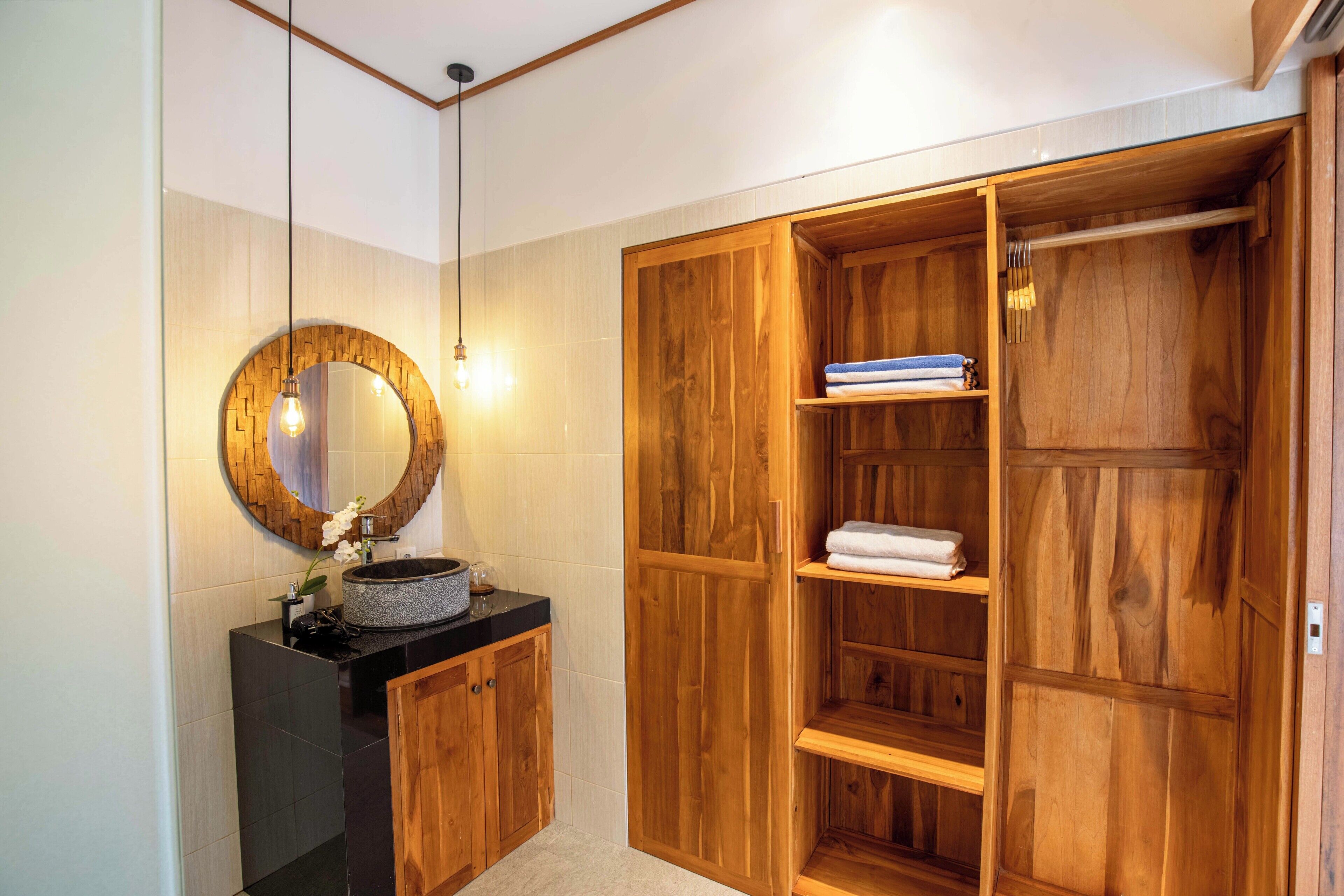 Un baño con tocador de madera, un espejo redondo y un armario empotrado de madera con estantes.