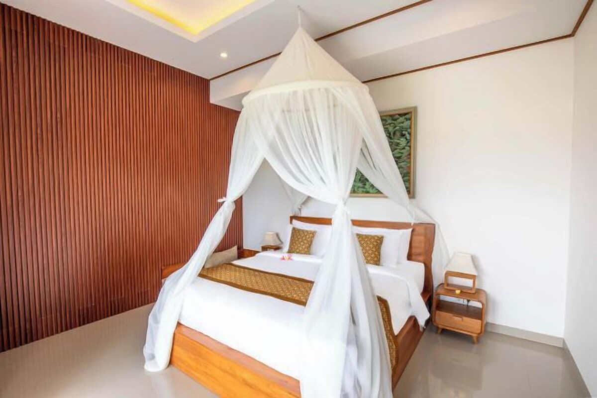 A modern bedroom with a canopy bed, wooden paneling on the wall, and a nightstand with a lamp.