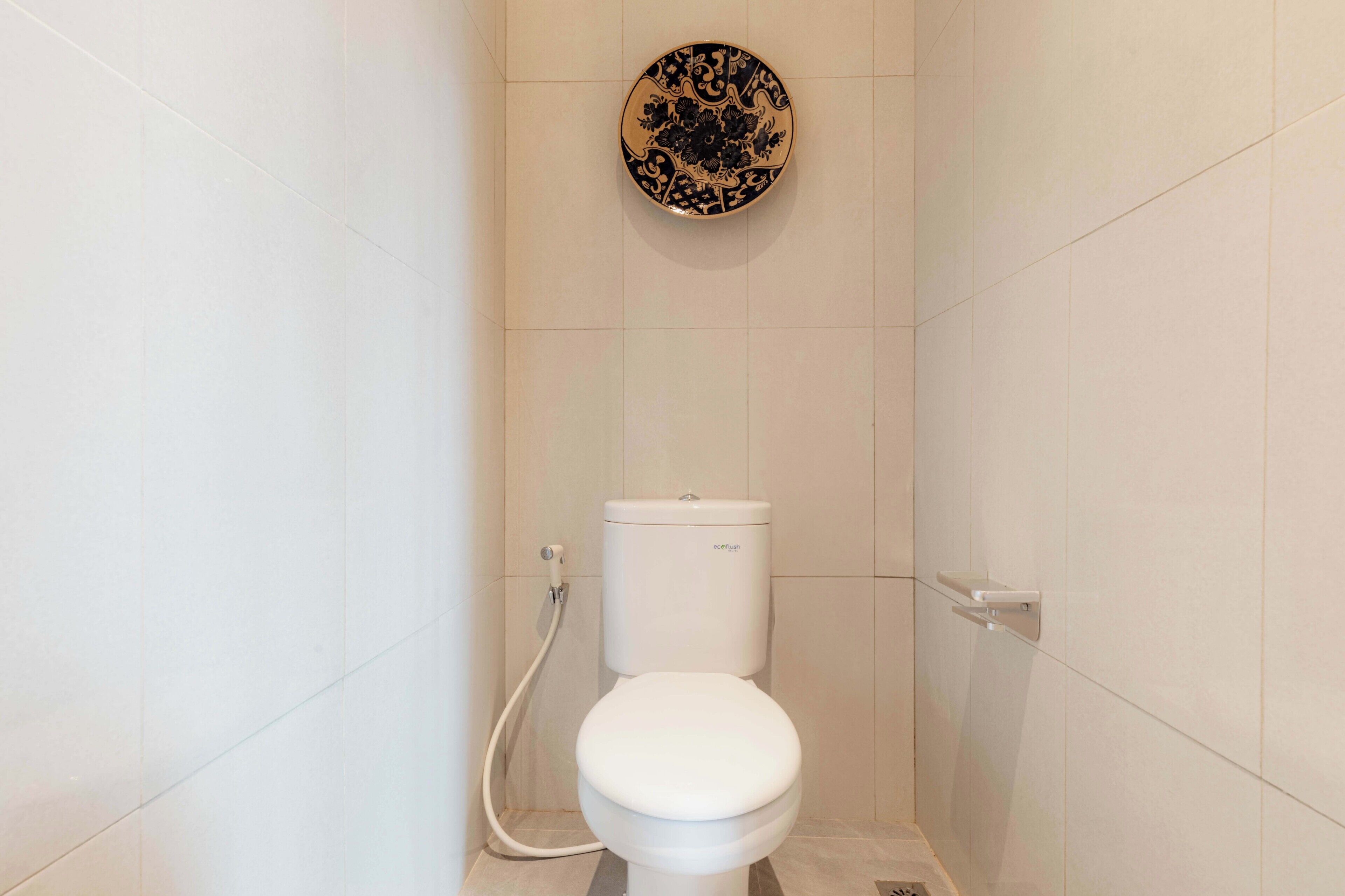 A small, modern bathroom with a white toilet, a wall-mounted sink, and a decorative plate above the toilet.