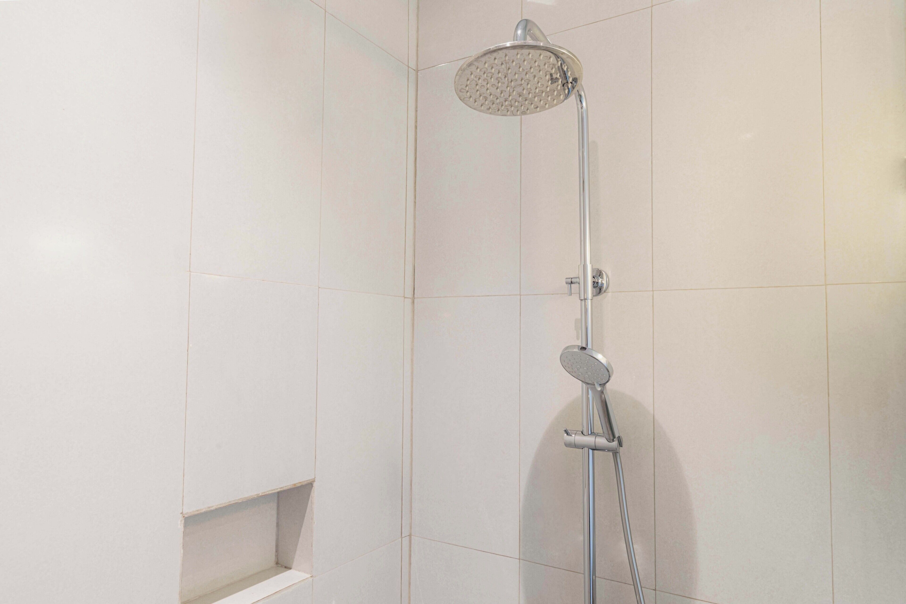 A shower with a handheld showerhead and a wall-mounted control panel.