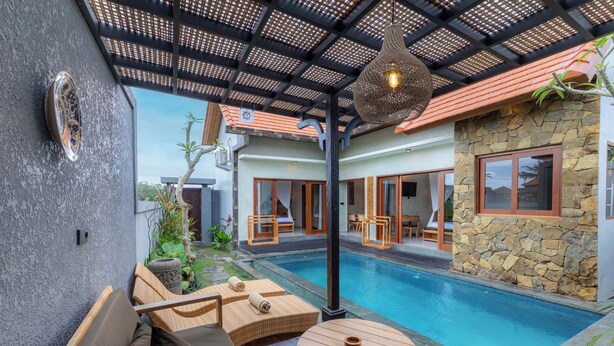 A poolside area with a covered seating area, a stone wall, and a view of the pool. - Weda Villas (Ubud)