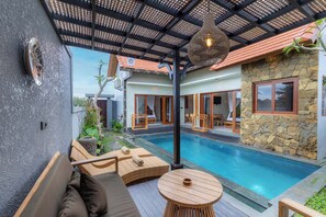 Un área junto a la piscina con un espacio de estar cubierto, una pared de piedra y vistas a la piscina.