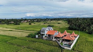 A large house with multiple red-roofed structures, surrounded by lush green fields and a distant mountain range. - Weda Villas (Ubud)