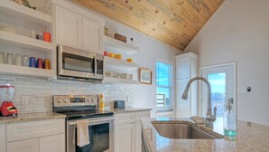 A modern kitchen with white cabinets, stainless steel appliances, a granite countertop, and a wooden ceiling. - Sleeps 46, 6 Homes | Private Boat Dock, Waterfront Pool, Views | Laguna Village (Corpus Christi)