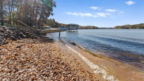 A lakeside view with a dock, wooden steps, and a gazebo. - Sunset Pointe by AvantStay | Waterfront, Beach, Fire Pit | Sleeps 14 | 5BDR 4BA (Troutman)